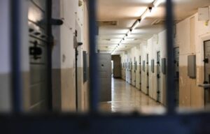 Zdjęcie przedstawia korytarz więzienny z otwartymi drzwiami do celi