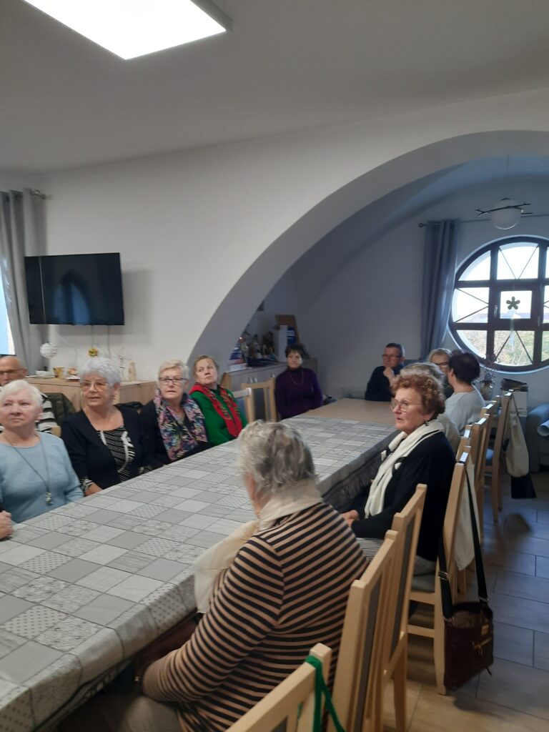 Zdjęcie przedstawia grupę seniorów siedzących przy długim stole
