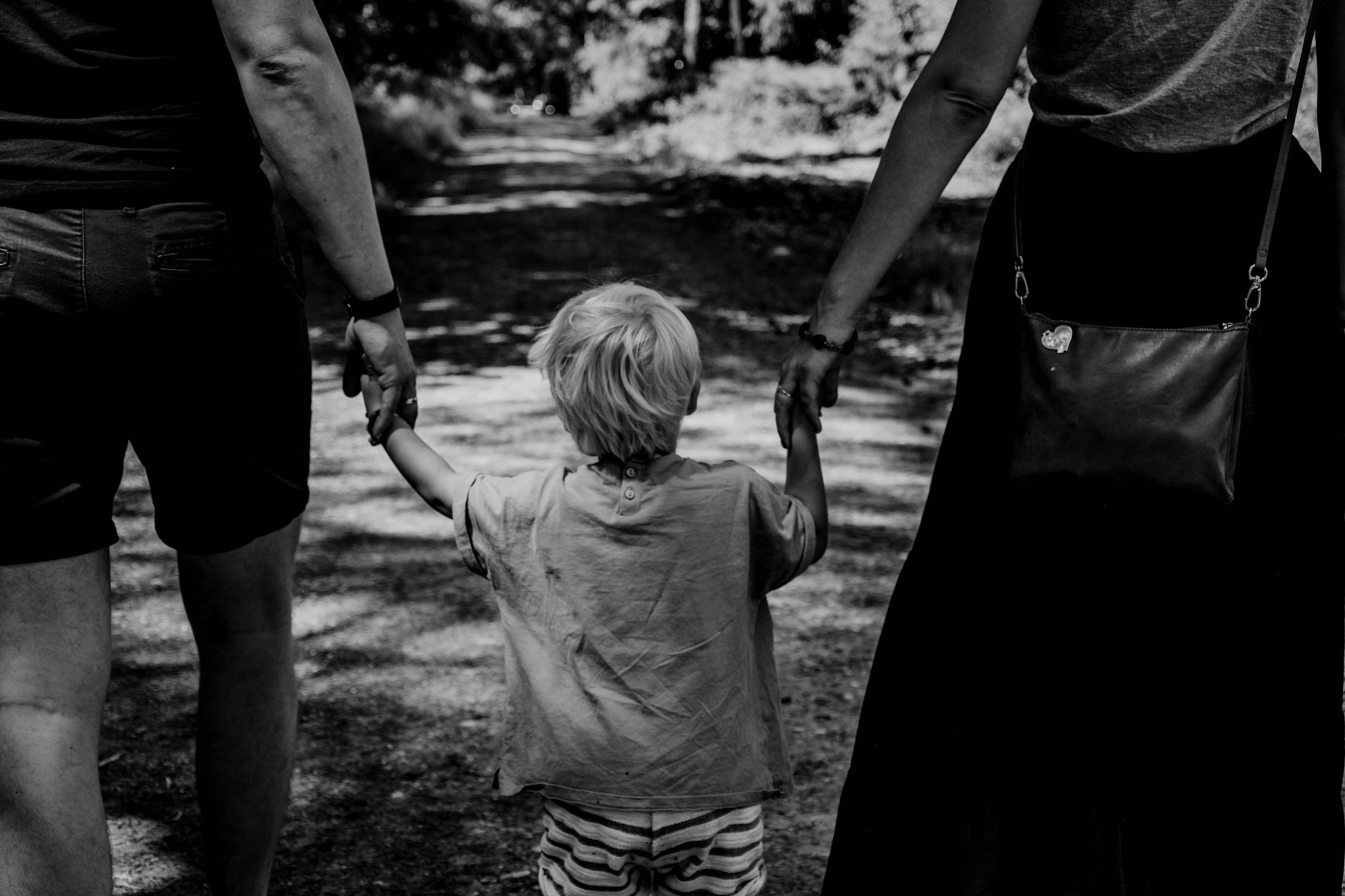 Zdjęcie przedstawia dziecko prowadzone za ręce przez rodziców.
